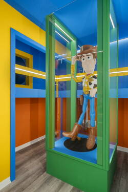 Welcome to a vibrant playroom with bold blue and sunny yellow walls featuring a giant toy figure. The playful design and clear display case invite you to relive childhood adventures in a whimsical atmosphere.
