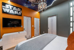 Discover a vibrant bedroom with a bold orange accent wall and a fun Star Wars theme. The sleek white furniture contrasts beautifully with rich colors, while ambient lighting from a unique chandelier adds a stylish flair.