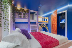 Enjoy a playful ambiance in this cozy bedroom, featuring vibrant blue walls, a plush red throw, and layered bedding for comfort. The charming lofted bed and soft lighting create an inviting and unique retreat for your stay.