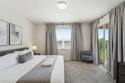 Rest in a bright and cozy bedroom with a comfortable bed, soft white bedding, gray accents, bedside lamps, abstract wall art, carpeted flooring, and a large window with natural light.