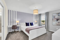 Bright and airy, this room features a stylish bed adorned with plush pillows and a soft throw, complemented by elegant striped walls. A cozy desk and modern lighting create an ideal spot for relaxation or planning your adventures.
