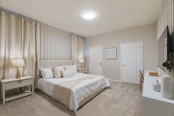 Rest in a serene bedroom with a cozy bed, tufted headboard, soft beige curtains, warm lamps, wall-mounted TV, and neutral decor, creating a calm space to relax during vacation.