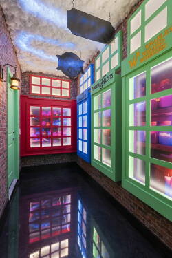 Step into a vibrant corridor with colorful, illuminated windows that add playfulness. The rich textures of exposed brick and glossy black flooring create an intriguing contrast, inviting you to explore further.