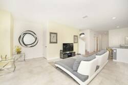 This bright and airy living room boasts a sleek, curved sofa with plush gray cushions, offering a stylish relaxation spot. A large mirror and framed art enhance the sophistication, while natural light elevates the modern feel.