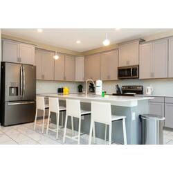 Cook and gather in a bright modern kitchen with gray cabinetry, stainless steel appliances, a large island, pendant lights, white bar seating, and clean neutral finishes.