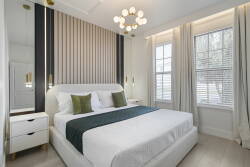Enjoy tranquility in this stylish bedroom, where natural light fills the space over a plush king-sized bed with rich green accents. The chic chandelier and sleek bedside tables create a serene atmosphere for your relaxation.