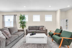 This bright, airy living room invites relaxation with a plush gray sofa and vibrant green armchairs. Natural light pours in through large windows, accentuating the soft textures and modern decor, ideal for leisurely afternoons.