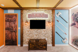 Welcome to our lively game room, where vibrant orange and blue walls meet rustic wooden accents. Enjoy the stunning stone wall backdrop and themed decor, including unique wall art and swords, adding character to your experience.
