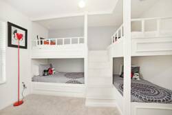 Bright and playful, this room features two charming bunk beds framed in crisp white, offering a cozy space for kids or guests. Vibrant accents, like the bold red lamp, complement the fun bedding, making this a delightful hideaway.