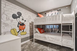 This cheerful kids' room boasts a stylish white bunk bed and a playful Mickey Mouse mural, creating a fun atmosphere. Soft gray tones enhance the vibrant accents, and plush carpeting ensures comfort for your little ones.