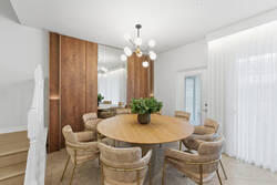 Gather in an elegant dining area with a round wooden table, soft upholstered chairs, modern chandelier, warm wood panels, mirror details, and white curtains, creating a bright space for family meals during vacation.