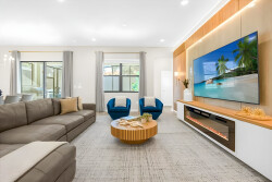 Enjoy relaxation in this stylish living room with soft gray sofas and rich wood accents. Plush blue chairs add a cozy touch, while large windows fill the space with natural light, creating a warm and inviting atmosphere.