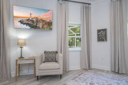 This cozy corner, filled with natural light, offers a plush armchair and an elegant side table, ideal for savoring your morning coffee. Soft neutral curtains frame the window, and vibrant coastal artwork adds a charming touch.