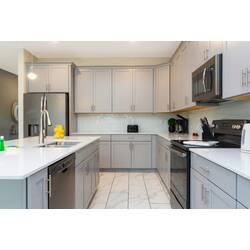 Cook with ease in a bright modern kitchen with gray cabinetry, stainless steel appliances, white countertops, a large island, pendant lighting, and clean neutral finishes.