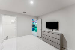 This bright bedroom combines a sleek gray dresser and a mounted TV for a cozy, functional feel. Crisp white bedding enhances the modern decor, while a playful splash of color from the adjoining room invites you to explore.