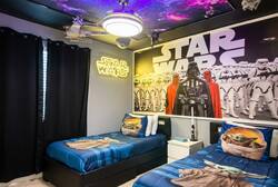 Rest in a Star Wars themed bedroom with two cozy twin beds, galaxy ceiling, neon sign, space decor, dark curtains, and bold wall art, creating an exciting space for kids during vacation.