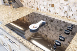 Enjoy culinary bliss in this stylish kitchen with a sleek black cooktop and rich granite countertops. The modern mosaic backsplash adds character, while elegant knobs ensure precision in every meal.