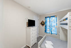 This cozy bedroom features a charming bunk bed alongside a sleek white dresser, creating a practical yet stylish sleeping area. Bright blue curtains frame the window, inviting natural light to enhance the welcoming atmosphere.
