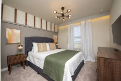 This cozy bedroom features a plush headboard and stylish bedside lamps for a warm ambiance. A soft, neutral palette is enhanced by a rich green throw, and large windows invite natural light, creating an inviting atmosphere.