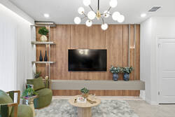 Relax in a stylish living room with a cozy sectional, green accent chairs, wall-mounted TV, warm wood feature wall, soft white curtains, modern lighting, and elegant decor for vacation moments.