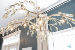 The striking chandelier, designed to resemble delicate branches, casts a warm glow across the room, enhancing the rich, deep wall color. Its unique textures and soft light create a cozy atmosphere, perfect for evenings in.