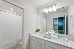 Refresh in a bright bathroom with a double vanity, large mirror, soft lighting, white cabinets, fresh towels, small decor accents, and a shower with a clean white curtain for vacation comfort.