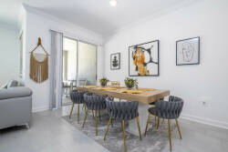 Enjoy the inviting ambiance at the sleek wooden dining table, surrounded by cozy gray chairs. The bright space, adorned with modern art and sliding glass doors, fills the room with natural light for a refreshing dining experience.