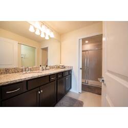 Refresh in a bright bathroom with a double granite vanity, large mirror, dark cabinets, warm lighting, soft rugs, and a glass shower for vacation comfort.