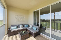 Relax on a covered balcony with cozy outdoor seating, sliding glass doors, wood-style flooring, and peaceful green views, creating a comfortable space to enjoy fresh air and quiet moments.