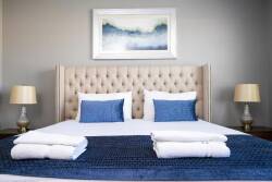 Discover a cozy ambiance in this beautifully styled bedroom, featuring a plush tufted headboard and soft, inviting linens. The calming blue tones and tasteful artwork create a tranquil atmosphere, perfect for restful nights.