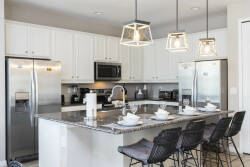 This stylish kitchen boasts sleek white cabinetry and a spacious granite island, ideal for gatherings. Contemporary pendant lights create a warm ambiance, and the stainless steel appliances enhance this inviting culinary space.