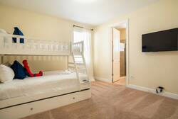 This cozy room features a charming bunk bed with crisp white linens, perfect for family adventures. Soft beige carpeting and warm yellow walls create a cheerful atmosphere, while a mounted TV offers entertainment for everyone.