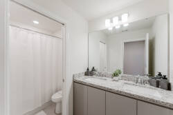 Experience a bright and inviting bathroom with sleek gray cabinetry and a spacious double vanity adorned with elegant granite. Enjoy the modern light fixture that enhances the well-lit atmosphere, making every detail feel fresh.