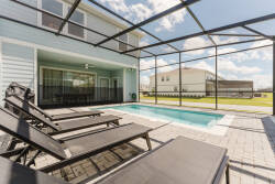 Step outside to unwind on sleek lounge chairs that surround your private pool, all framed by a stylish screened enclosure. The bright blue sky and spacious yard invite relaxation, offering a perfect spot for sun-soaked afternoons.
