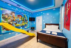 Sleep in a playful Toy Story themed bedroom with bright blue walls, cloud details, a yellow slide, wall-mounted TV, colorful murals, and cozy bedding for a fun family stay.