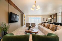 Relax in a stylish open living area with a large sofa, green accent chairs, wall-mounted TV, warm lighting, wood details, and a dining space, creating a bright and comfortable place to gather during your vacation.