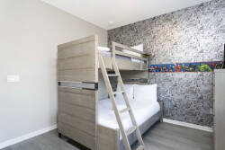 This charming bunk room boasts a stylish wooden bunk bed, ideal for families or groups, and a playful accent wall with colorful artwork. Natural light brightens the space, ensuring a cheerful and restful atmosphere for your stay.