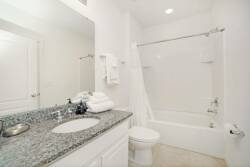 This bright, airy bathroom boasts a sleek granite countertop and modern fixtures that enhance its clean, white look. Plush towels add comfort, while a spacious tub beckons you to unwind after a day of exploration.