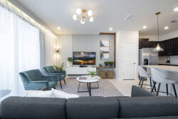 Welcome to a bright living area filled with natural light, showcasing cozy teal chairs and modern decor. The open layout connects effortlessly to a stylish kitchen, perfect for relaxation and entertainment. Enjoy your stay!