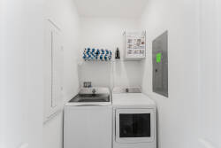 Step into a clean and functional laundry area, featuring a spacious washer and dryer set against crisp white walls. Convenient shelving and neatly organized supplies ensure you have everything you need for a hassle-free stay.