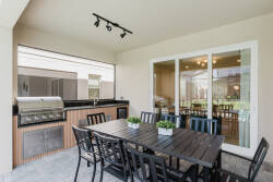 Savor outdoor dining in this spacious area with a stylish wooden table, comfy black chairs, and a modern grill. Large windows flood the space with natural light, enhancing your meal experience.