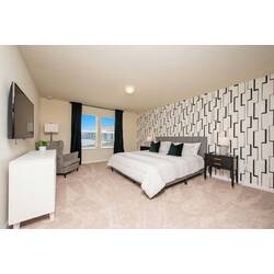 Rest in a spacious bedroom with a cozy white bed, geometric accent wall, black nightstands, wall-mounted TV, soft carpet, dark curtains, and a comfy chair for vacation comfort