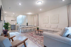 Step into a cozy living room adorned with soft neutrals and a plush area rug, where natural light pours in from the large windows. The sleek sectional invites relaxation, while tasteful artwork adds a touch of sophistication.