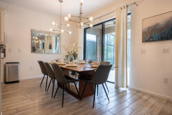 Enjoy the warm ambiance of the modern chandelier above the inviting dining table, surrounded by sleek black chairs. Natural light pours in through the expansive glass doors, blending indoor comfort with beautiful outdoor views.