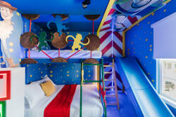 This lively children's room boasts a cheerful mix of bright blues and reds, with fun character murals. A unique bunk bed with a slide sparks adventure, while cozy bedding promises a restful night for your little ones.