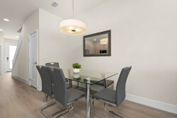 Bright and airy, this dining area features a sleek glass table surrounded by contemporary grey chairs, perfect for shared meals. A stylish pendant light casts a warm glow, while a touch of greenery adds a refreshing accent.