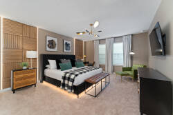 Enjoy a stylish bedroom with a plush king bed, a chic black headboard, and warm wood accents. Large windows fill the space with natural light, showcasing modern decor and a cozy reading nook for your relaxation.