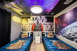 Rest in a Star Wars themed bedroom with two cozy twin beds, galaxy ceiling, neon sign, space decor, dark curtains, and bold wall art, creating an exciting space for kids during vacation.