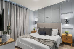 Rest in a modern bedroom with a cozy bed, gray accent wall, soft curtains, wall-mounted TV, warm wood nightstands, and gentle lighting, perfect for relaxing during vacation.