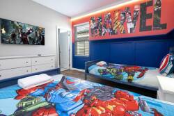 This vibrant bedroom with superhero-themed bedding and bold blue walls creates a playful retreat, featuring a striking "MARVEL" mural and a large TV for cozy movie nights that everyone can enjoy.
